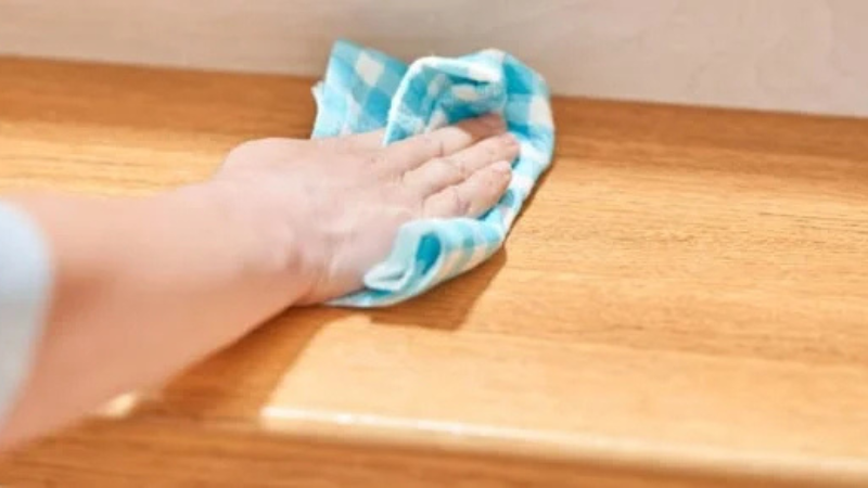 Main essuyant une surface en bois avec un chiffon à carreaux bleus.